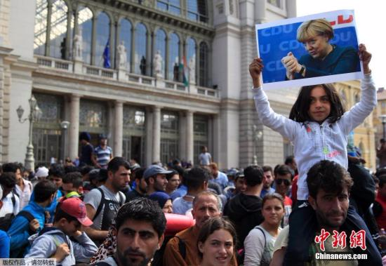 在匈牙利布达佩斯的一处火车站外，大量难民徒步前往匈奥边境，准备从奥地利前往德国。一名小女孩双手高举德国总理默克尔的照片。