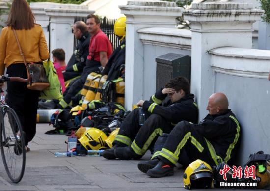 6月14日，伦敦西部一栋24层的公寓楼发生大火，火势猛烈，蔓延到了所有楼层。目前这场火灾已造成超过50人受伤。图为疲惫的消防员在路边休息。 <a target='_blank' href='http://www.chinanews.com/'></table>中新社</a>记者 周兆军 摄
