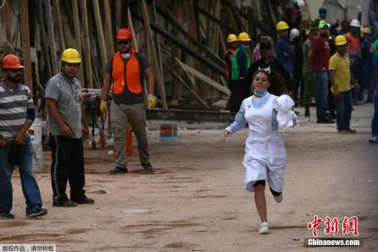 一名护士在救援现场飞奔而过，她只是数千名专业人士和志愿者中的一员。在这次强震中，墨西哥城多所学校坍塌，部分学生没能逃离，救援工作还在继续。