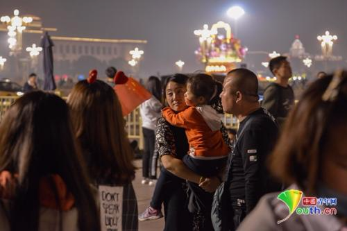 一位小女孩在母亲的怀中手持国旗等着看升旗。 中国青年网记者 李永鹏 摄影
