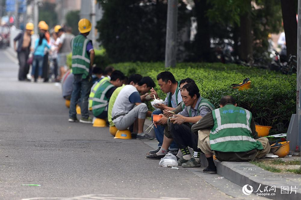 中午时分，CBD附近工地的施工人员在路边就餐。（人民网记者 翁奇羽 摄）